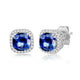 Load image into Gallery viewer, Jewelili 10K White Gold with Cushion Cut Created Blue Sapphire and 1/10 CTTW Round Natural White Diamonds Halo Stud Earrings
